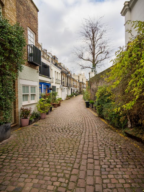 A residential street in Kensington featuring red-brick Victorian-style buildings with ornate architectural details and bay windows. The sidewalk is clean and well-maintained, lined with black iron rai